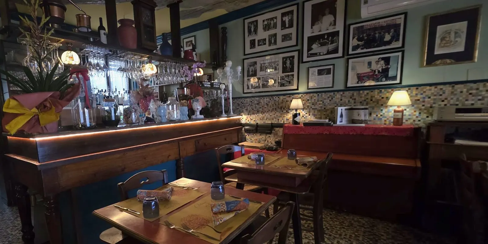 La sala dell'osteria con il bancone, le bottiglie e le sedie rosse