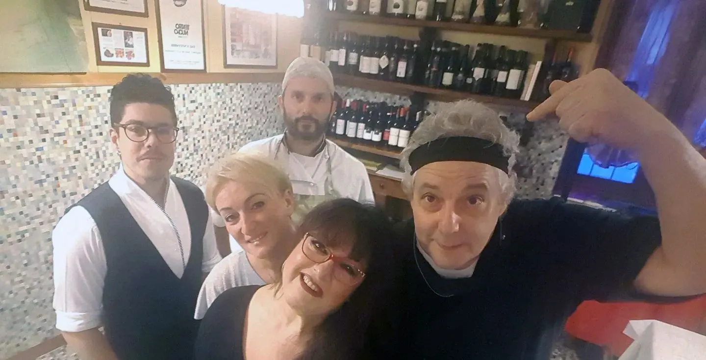 Lo staff dell'Osteria dell'Olmo sorride davanti agli scaffali dei vini